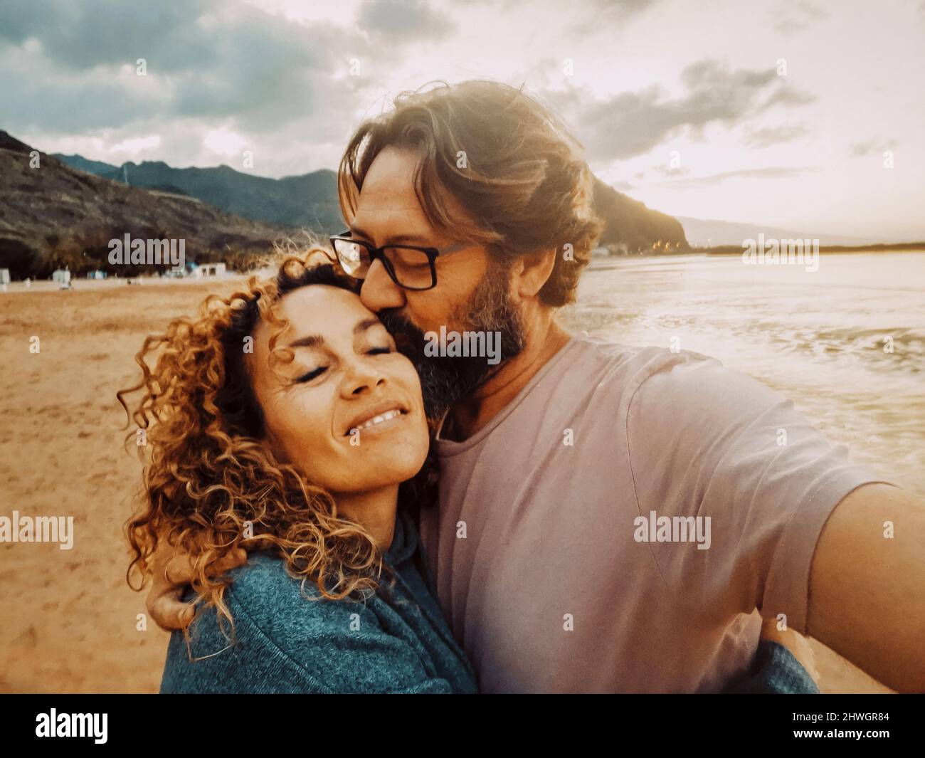 Happy adult couple in love enjoy leisure summer holiday vacation together taking selfie picture with mobile phone. Man kissing woman smiling. Man and Stock Photo