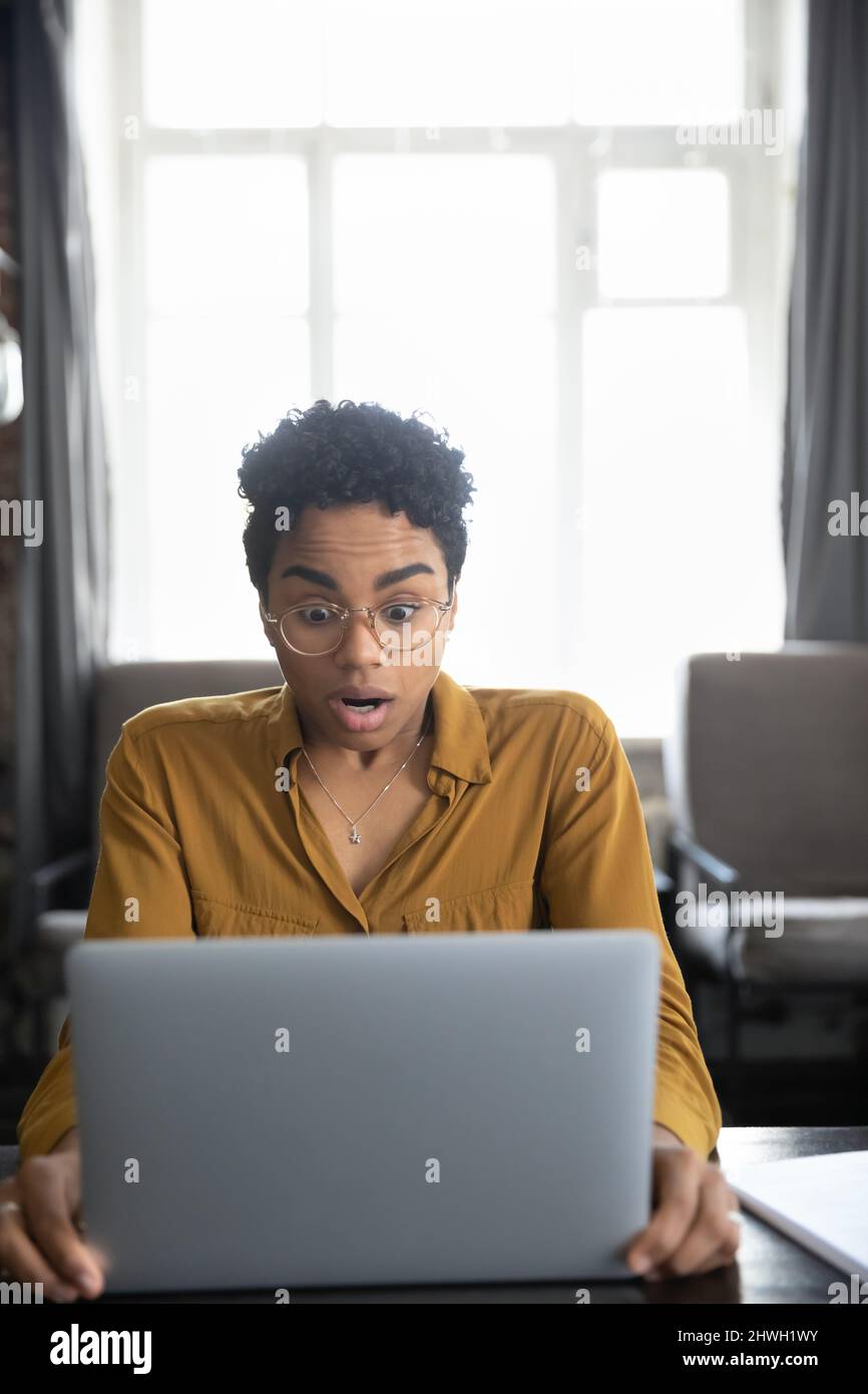 Surprised shocked millennial Black girl looking at computer display Stock Photo