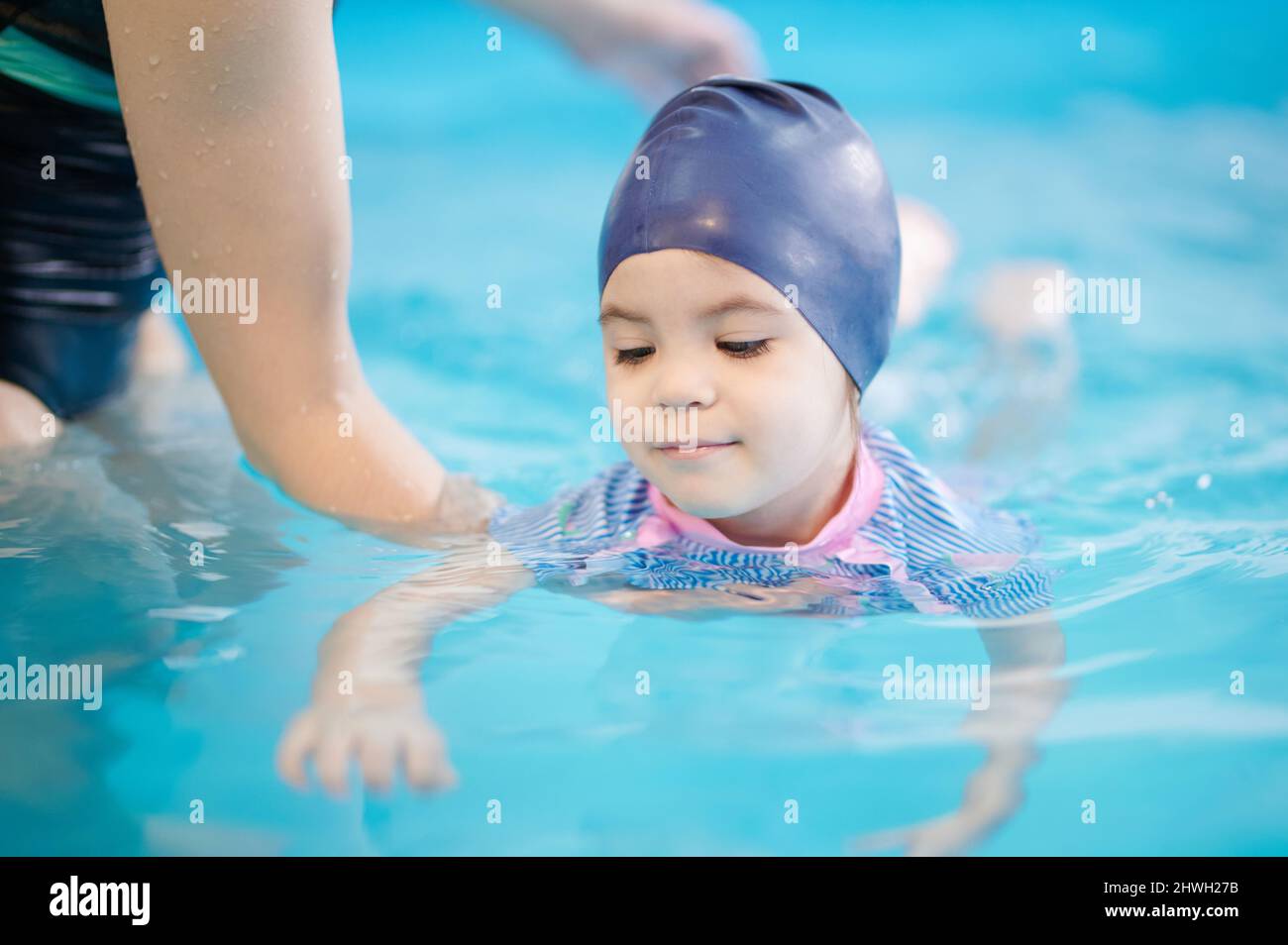 Infant learning to swim with adult help on blurred pool water Stock