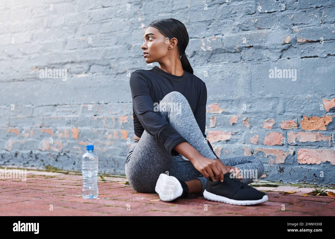 Another day, another fitness goal to slay. Shot of a young woman tying her shoelaces before a workout session. Stock Photo