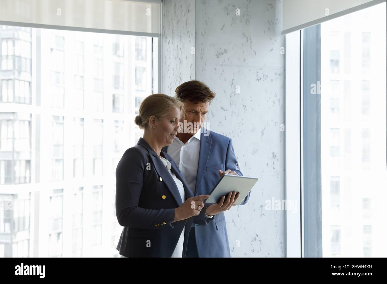 Focused two middle aged colleagues using digital tablet. Stock Photo