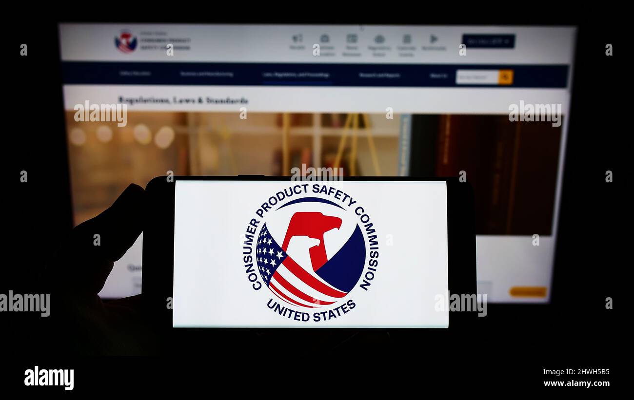 Person holding smartphone with logo of United States Consumer Product Safety Commission on screen in front of website. Focus on phone display. Stock Photo