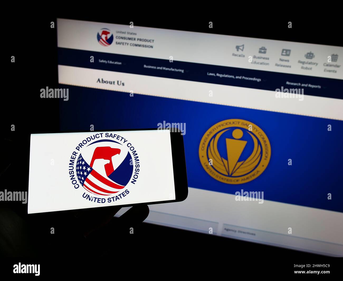 Person holding cellphone with logo of United States Consumer Product Safety Commission on screen in front of webpage. Focus on phone display. Stock Photo