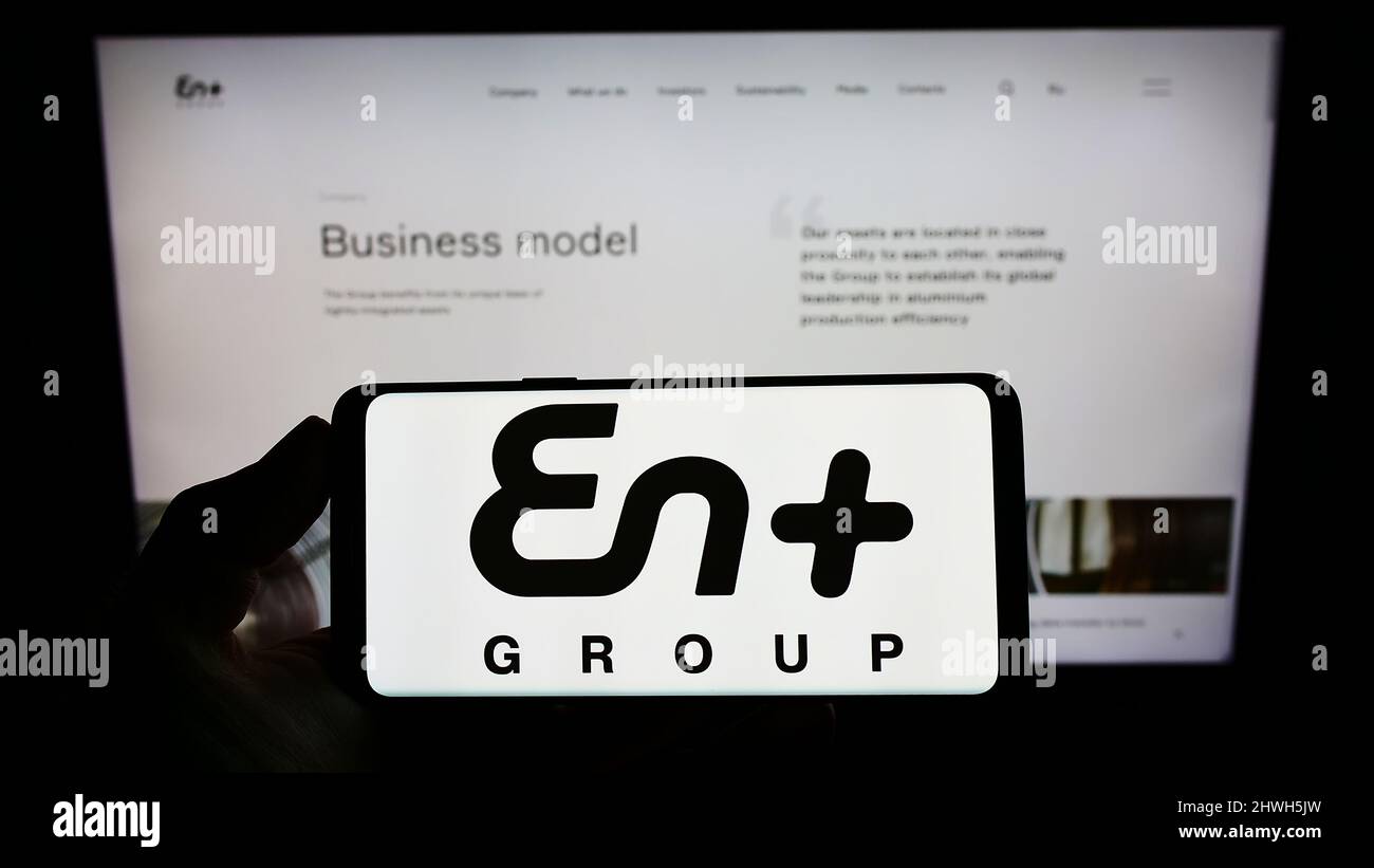 Person holding cellphone with logo of Anglo-Russian company En+ Group plc on screen in front of business webpage. Focus on phone display. Stock Photo
