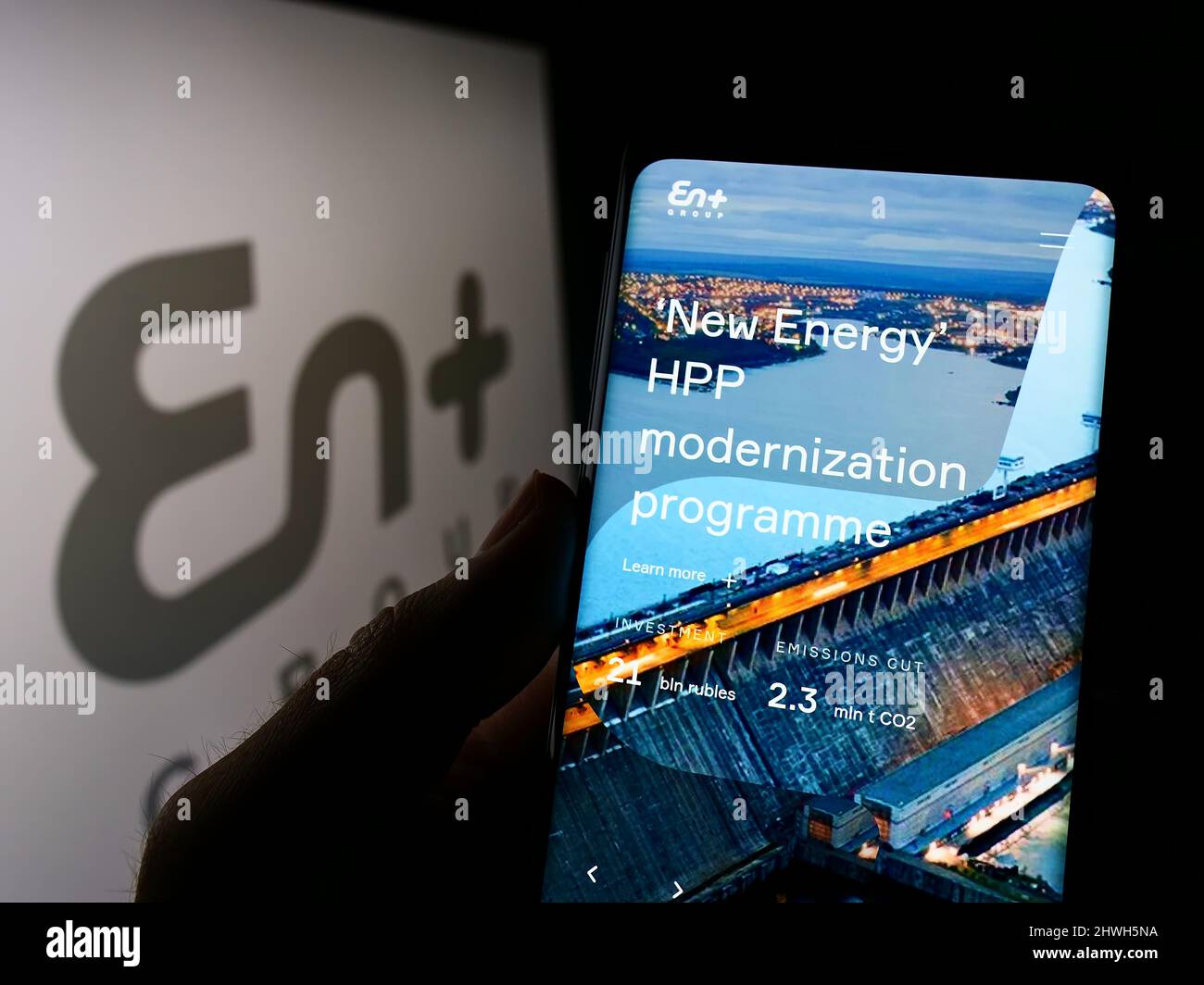 Person holding cellphone with website of Anglo-Russian company En+ Group plc on screen in front of logo. Focus on center of phone display. Stock Photo