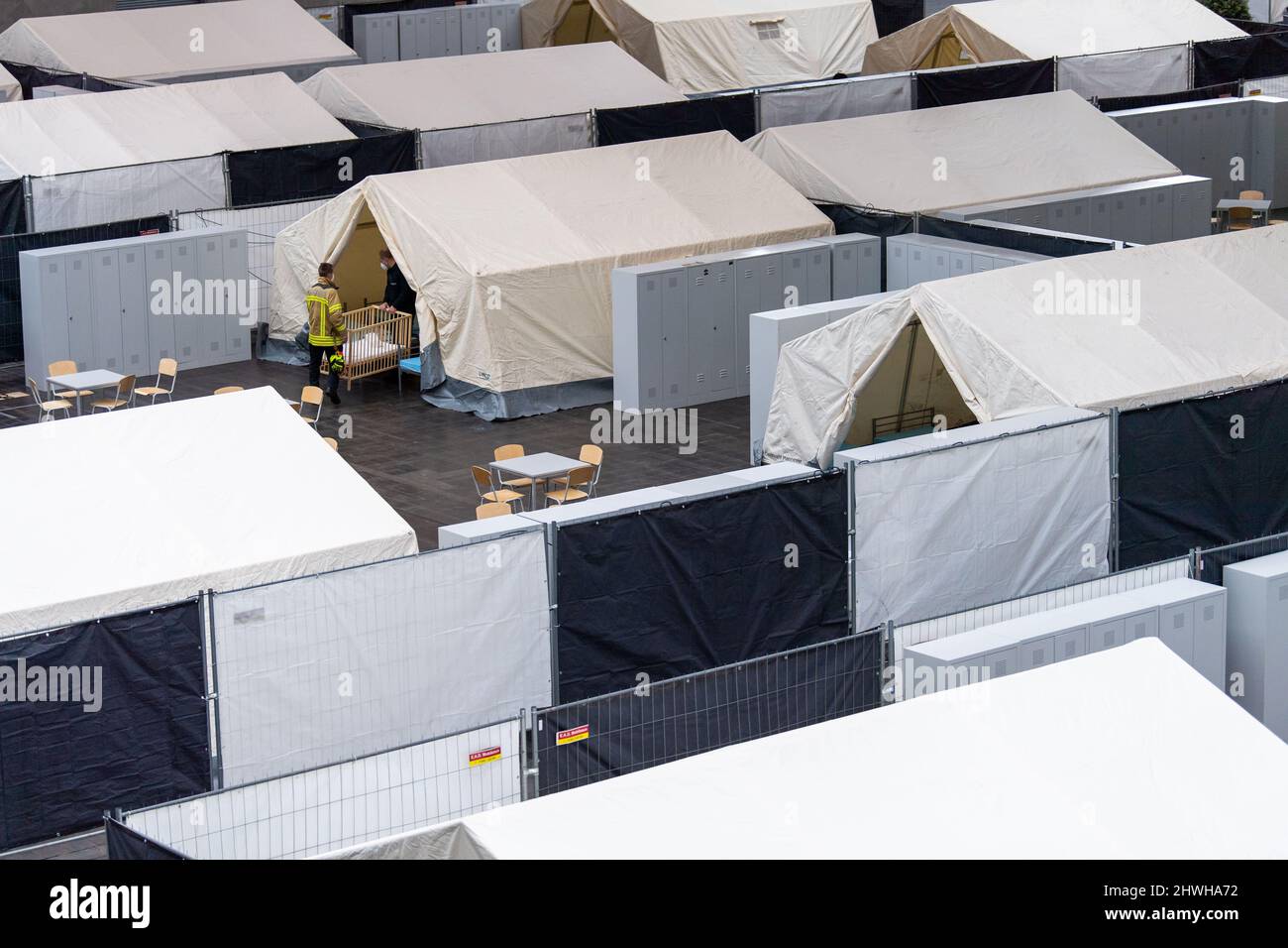Hanover, Germany. 06th Mar, 2022. Firefighters carry a baby crib into a tent. The city of Hanover, in cooperation with Deutsche Messe AG, is preparing a shelter for refugees from the Ukraine crisis on the exhibition grounds. Credit: Lino Mirgeler/dpa/Alamy Live News Stock Photo
