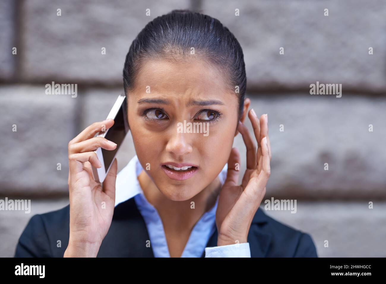 I cant quite hear you. A shot of a young businesswoman having trouble hearing on her cellphone. Stock Photo