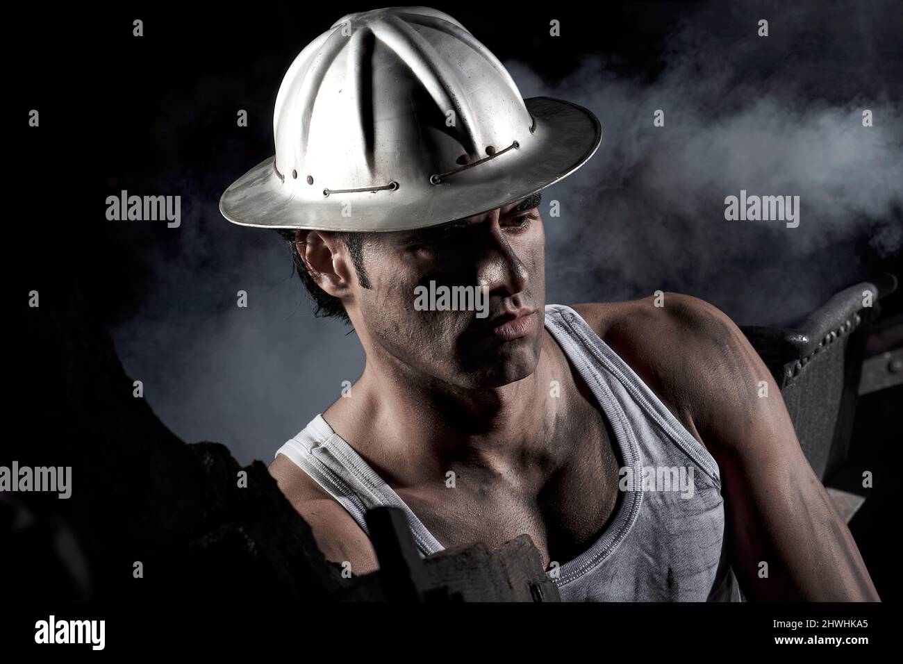 Worker inside a mine stained with ore and wearing a short-sleeved t-shirt and old aluminum helmet Stock Photo