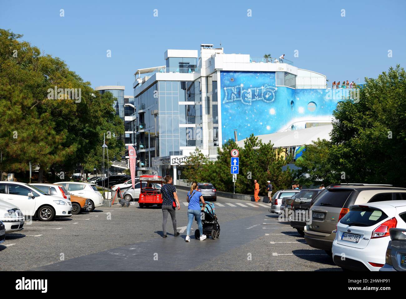 ODESA, UKRAINE - SEPTEMBER 25: The young family with baby carriage goes from car parking to Nemo Odessa dolphinarium. It is located on Lanzheron beach Stock Photo