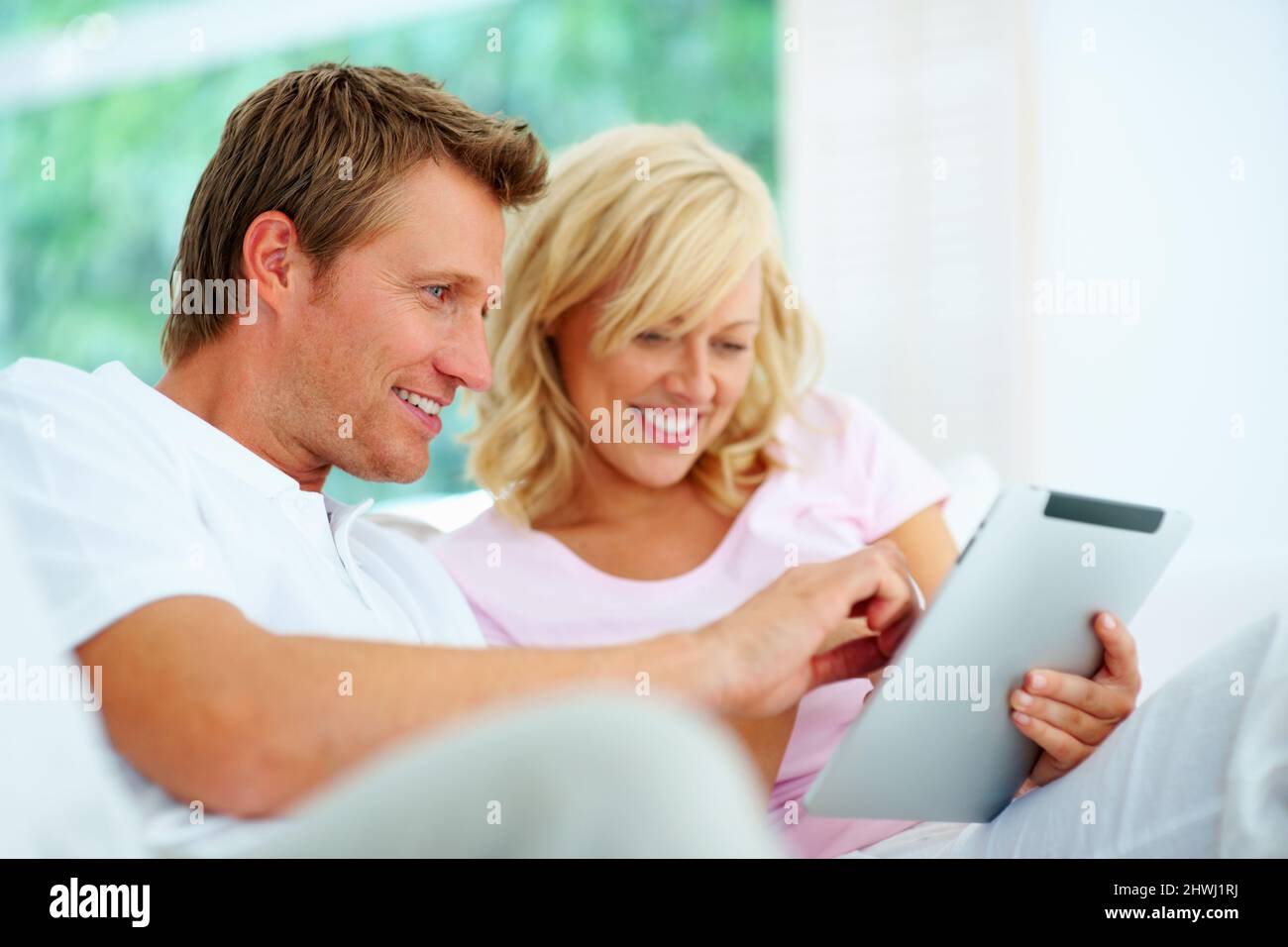 Happy couple using tablet pc. Happy couple sitting on a sofa using tablet pc. Stock Photo