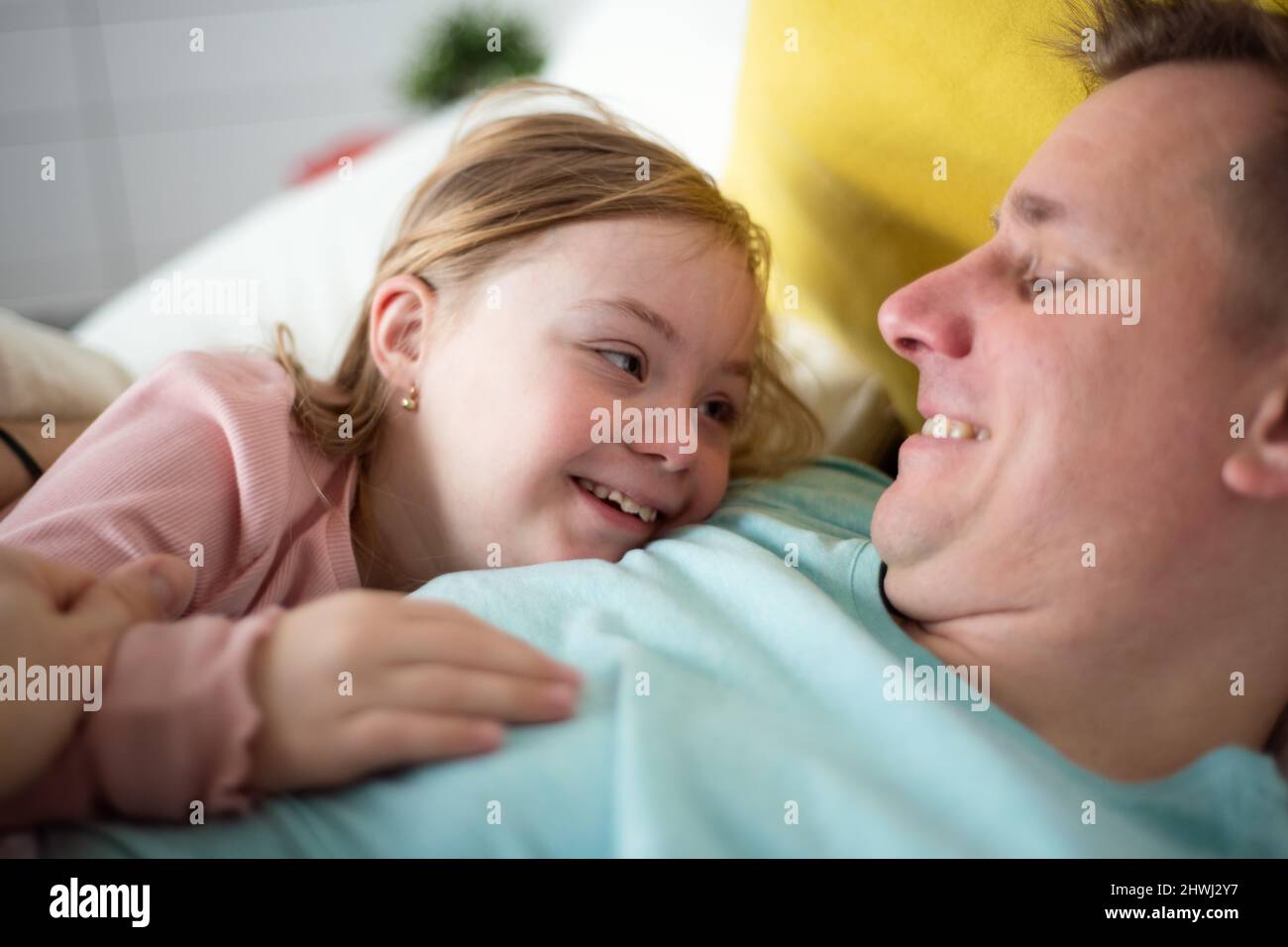 Father with hugging his little daughter with Down syndrome on bed at home. Stock Photo