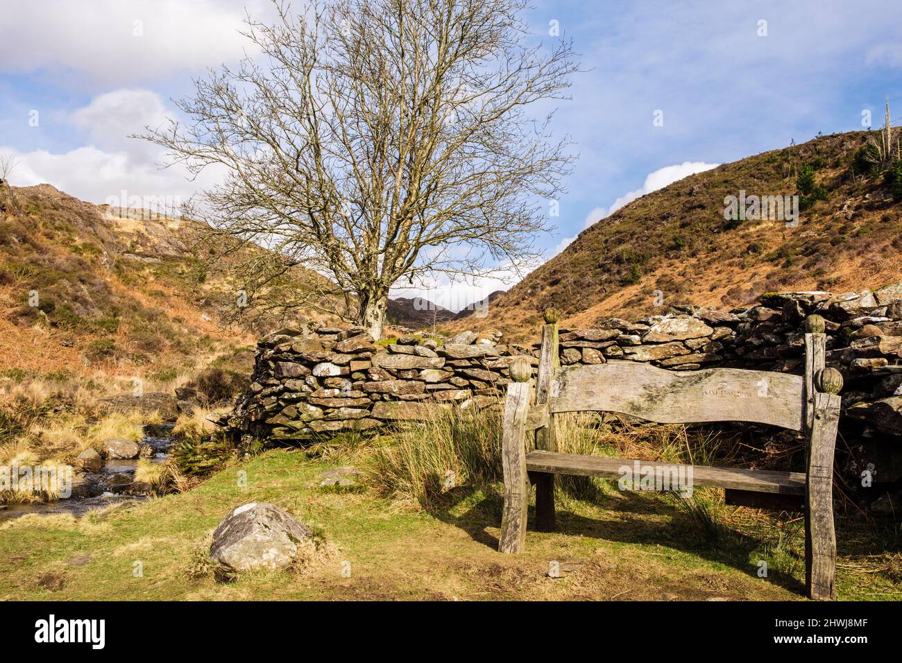 Empty bench seat by a stone wall and stream in Cwm Bychan in Snowdonia National Park. Beddgelert, Gwynedd, north Wales, UK, Britain Stock Photo