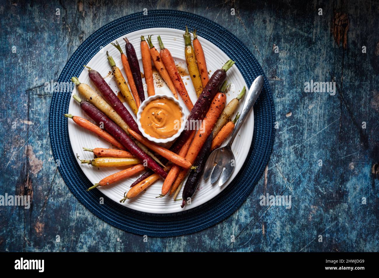 A round dish filled with roasted rainbow carrots and sriracha mayo dip. Stock Photo