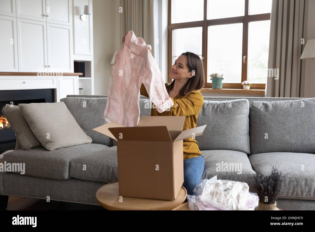 Smiling woman unpack parcel with delivered online fashion clothes Stock Photo