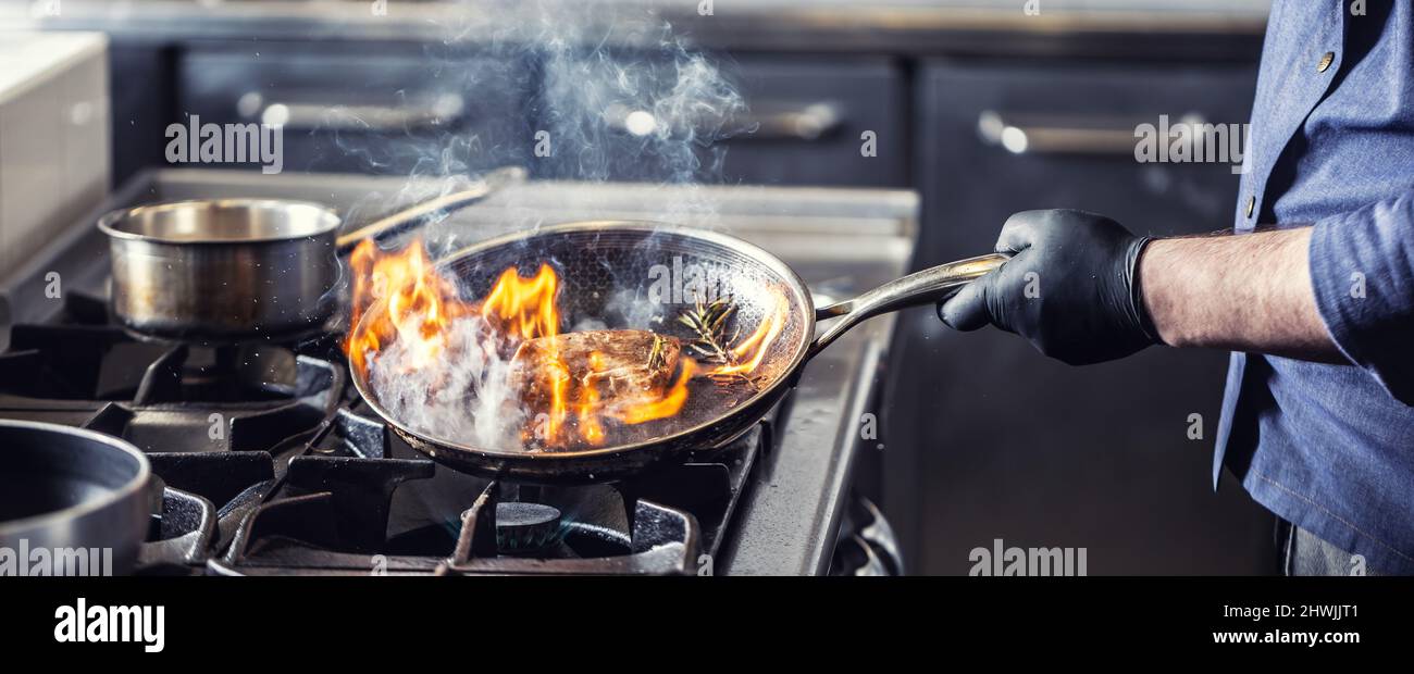 Chef in the kitchen leans pan to the side for alcohol in it to catch