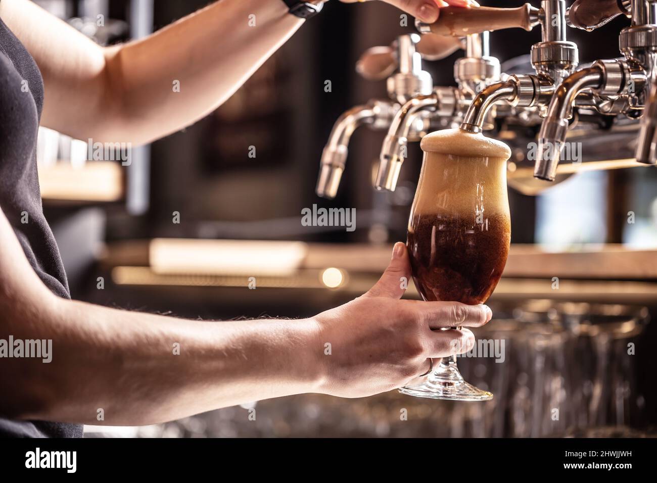 Foam on dark beer is about to pour out of the glass tapped with the