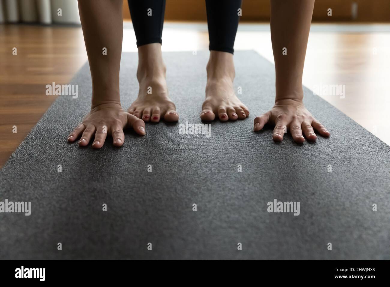 Woman standing on mat performs Uttanasana, palms and feet closeup Stock Photo