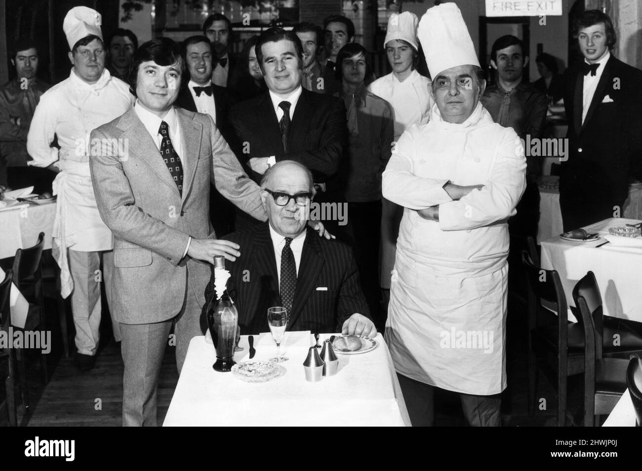 Vesuvio owners Mario Romano, Umberto Cavaldoro and Enzo Rippa, surrounded by their staff stand over William Gallone who is about to sample the restaurant's dishes.9th April 1973. Stock Photo