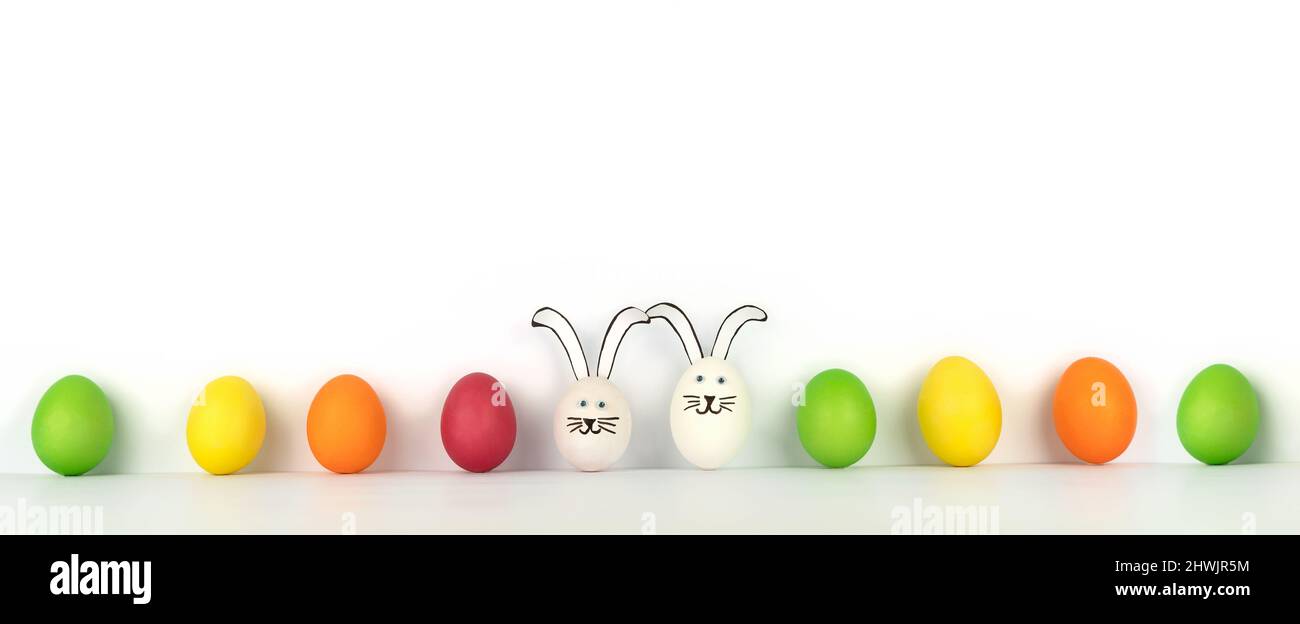 Happy Easter. Creative banner from multi-colored eggs in row and two funny rabbits. White background Stock Photo