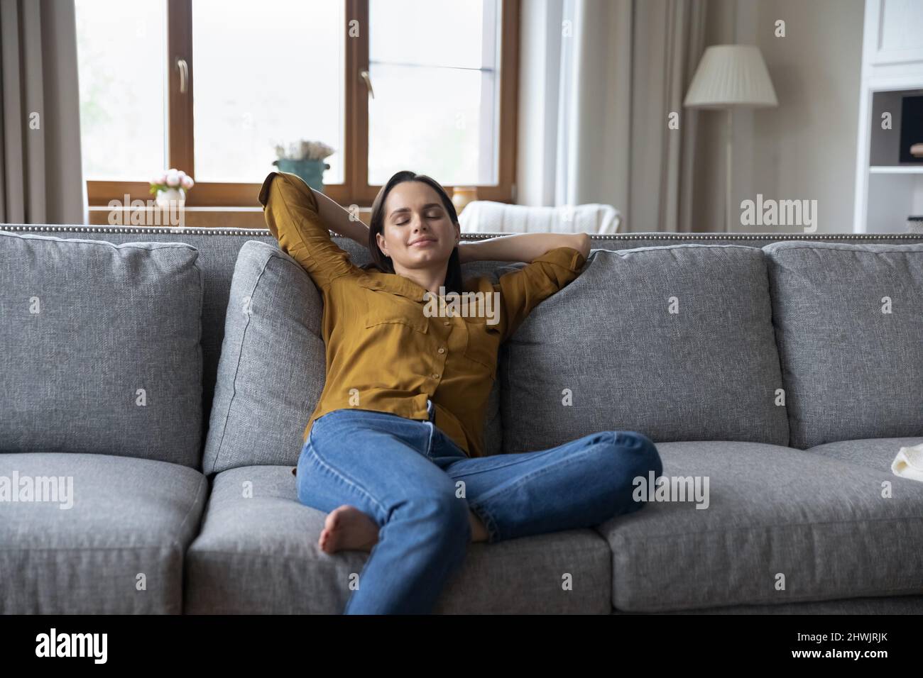 Serene young woman relaxing on couch in cozy living room Stock Photo