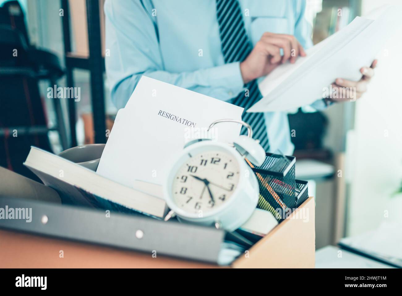 cardboard box and resignation letter, dossier, alam clock, coffee cup, calculator and drawing tube in box. Quiting a job, businessman fired or leave a Stock Photo