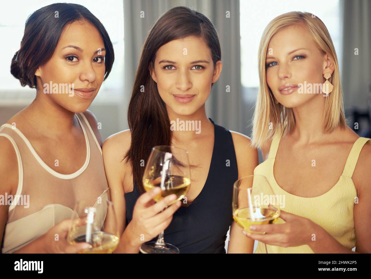 Shopping for clothing at an exclusive store. Portrait of three beautiful young women drinking white wine together. Stock Photo