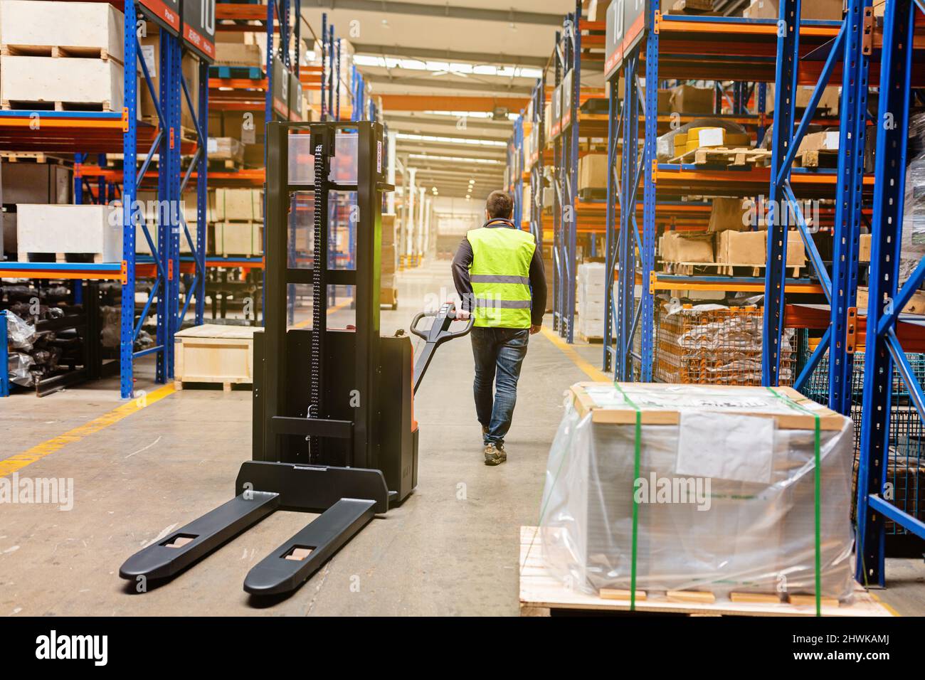 Storehouse man employee in uniform using forklift with box in modern