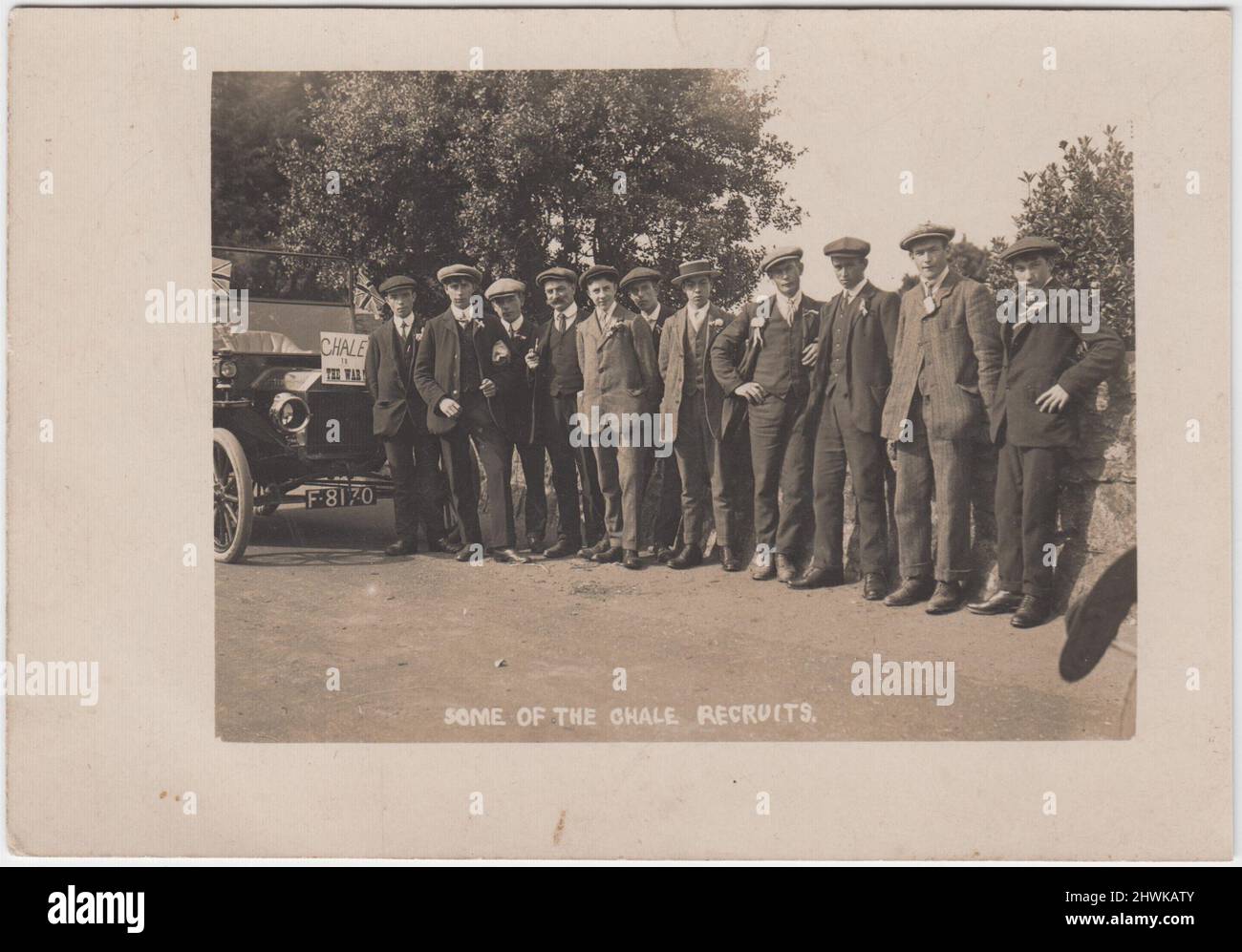 'Some of the Chale recruits': photograph of army volunteers in the early months of the First World War in the village of Chale, Isle of Wight. It shows a line of mostly young men in suits and hats (flat caps & a straw boater), with ribbons, etc., in their button holes. They are standing next to a car with the registration number F8170 which has been decorated with two Union Jacks and a sign which says 'Chale to the War' Stock Photo