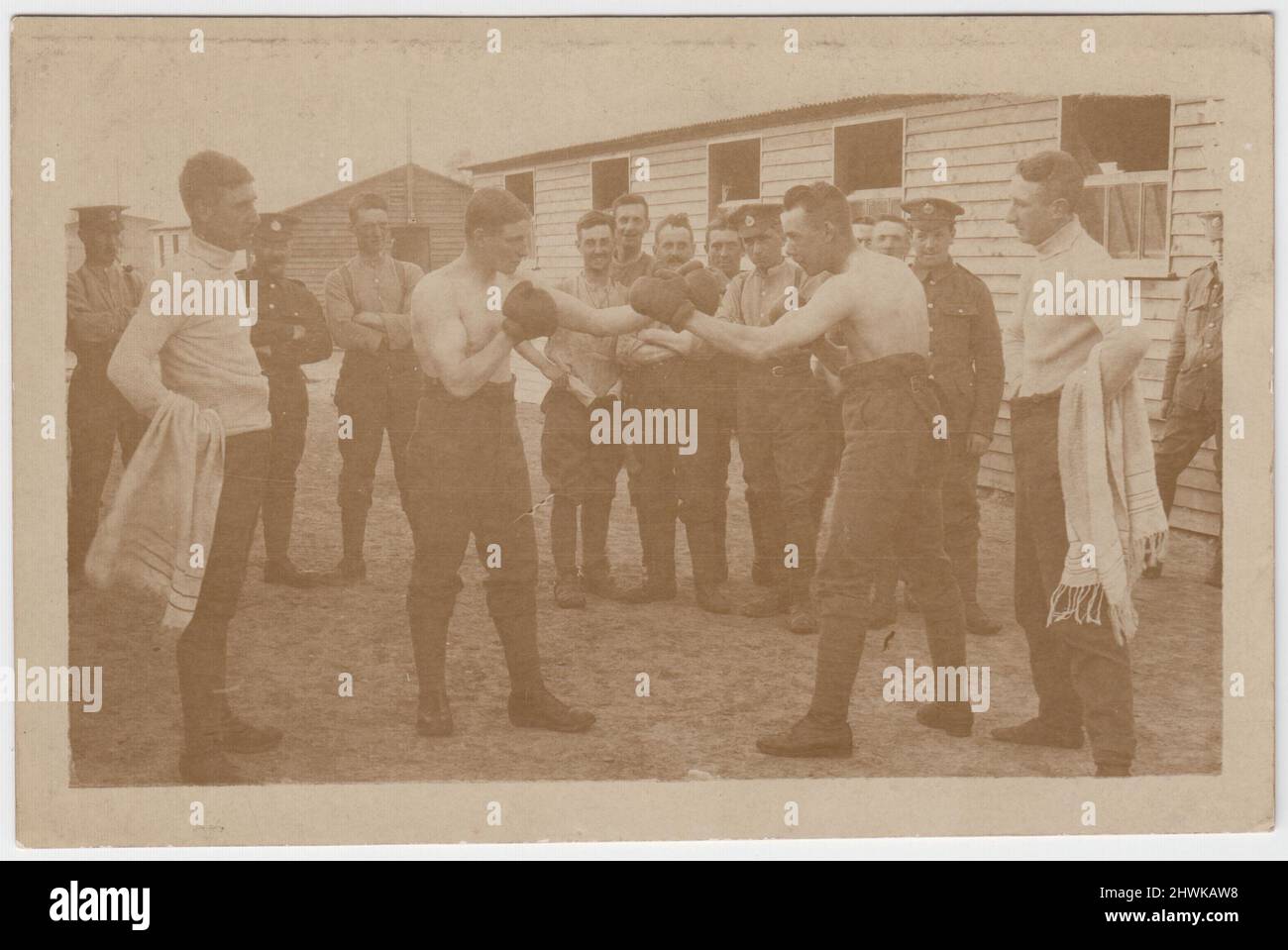Army boxing match in a camp of the Royal Engineers, early 20th century. Two soldiers, stripped to the waist & wearing boxing gloves, are sparring. They are watched by their seconds, carrying towels, and a small group of soldiers. Barracks huts can be seen in the background of the photograph Stock Photo