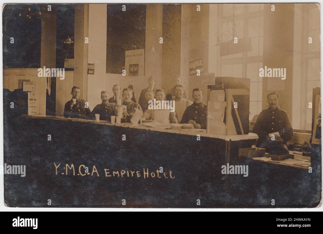 Young Men's Christian Association (YWCA) Empire Hotel, First World War: Photograph of the inside of a YWCA hotel, hut or hostel. The image shows a long counter with men standing behind, most in army uniform. There are notices which say 'Post Office', 'Change given' and adverts for Horlicks malted milk and lunch tablets Stock Photo