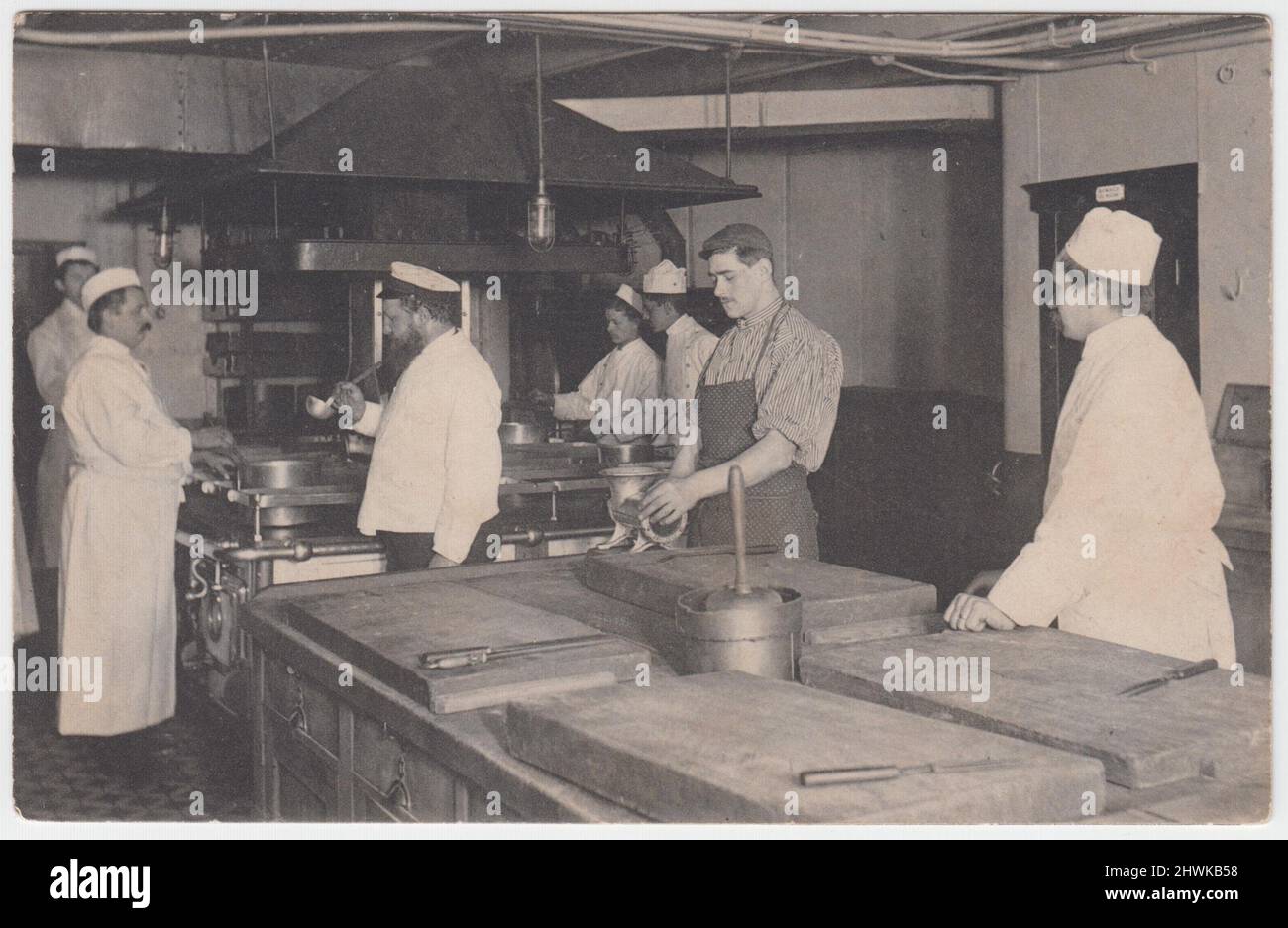 'The first kitchen on board a fast steamer' / 'Die erste Küche an Bord eines Schnelldampfers': German postcard showing men at work in a ship's kitchen, with stoves, mincer, butchers' blocks and knives. The image dates from the first decade of the 20th century Stock Photo