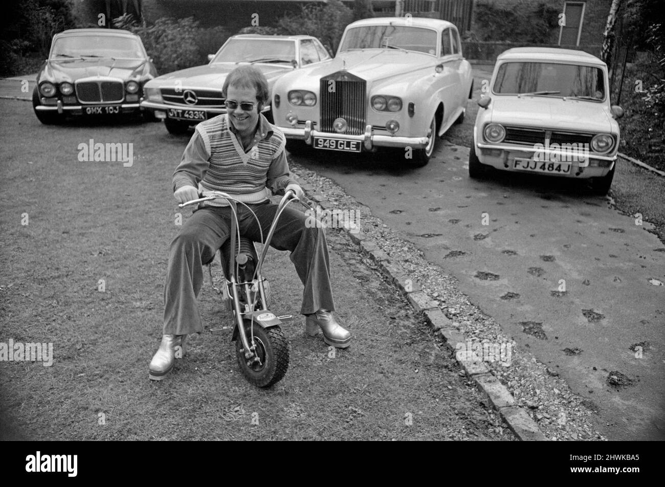 Elton John pictured at his home, sitting on a small motorbike in front of four of his cars.His cars include a Mercedes (2nd left) and a white Rolls Royce (3rd left)  Picture taken 4th April 1972 Stock Photo