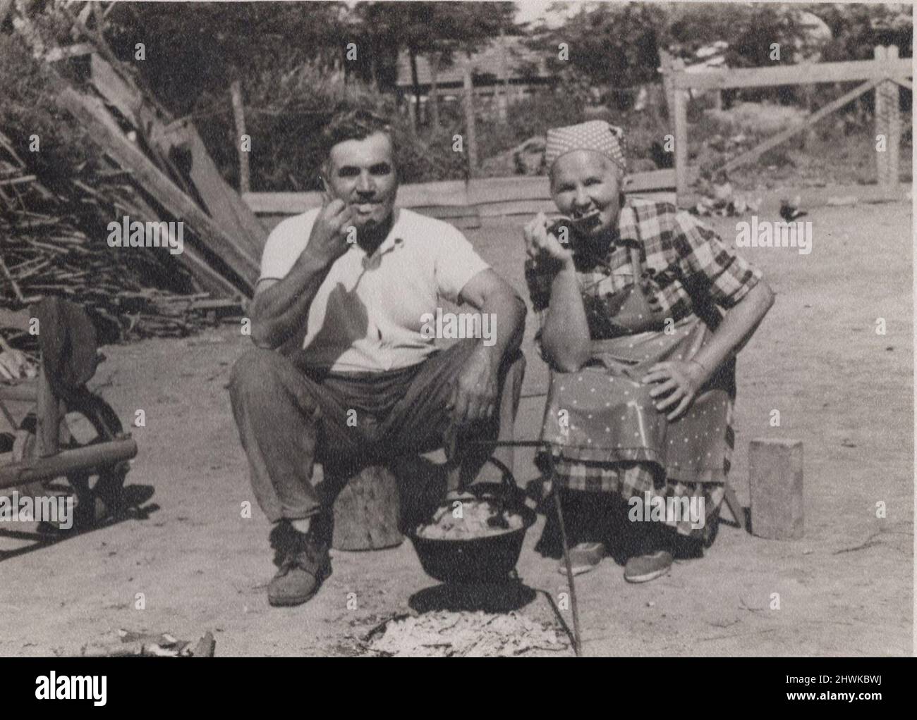 vintage black and white photo about a mid ages man sitting with one older lady outside and having  lunch togedher. Possibly they are mother and son. They are cooking and eating a dish what called in hungarian language: bogrács. Might be theay are eating gulash / gulyás. Period: 1930s. Source. original photograph. ADDITIONAL-RIGHTS-CLEARANCE-INFO-NOT-AVAILABLE Stock Photo