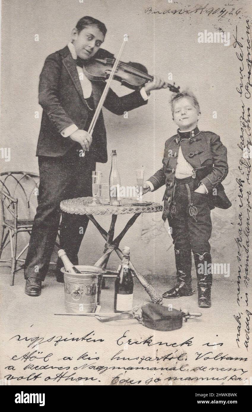 antique black and white  postcard picture from 1890s about a child hussar and his musician ( gipsy violist) are celebrating togedher with bottles of champagne, smoking cigarette  and singing songs. ADDITIONAL-RIGHTS-CLEARANCE-INFO-NOT-AVAILABLE violin close up / vintage man smoking a cigarette Stock Photo