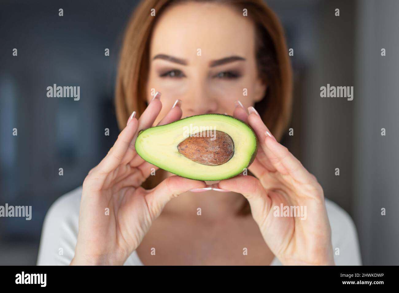 Young Caucasian woman showing halved avocado, depth of field Stock Photo