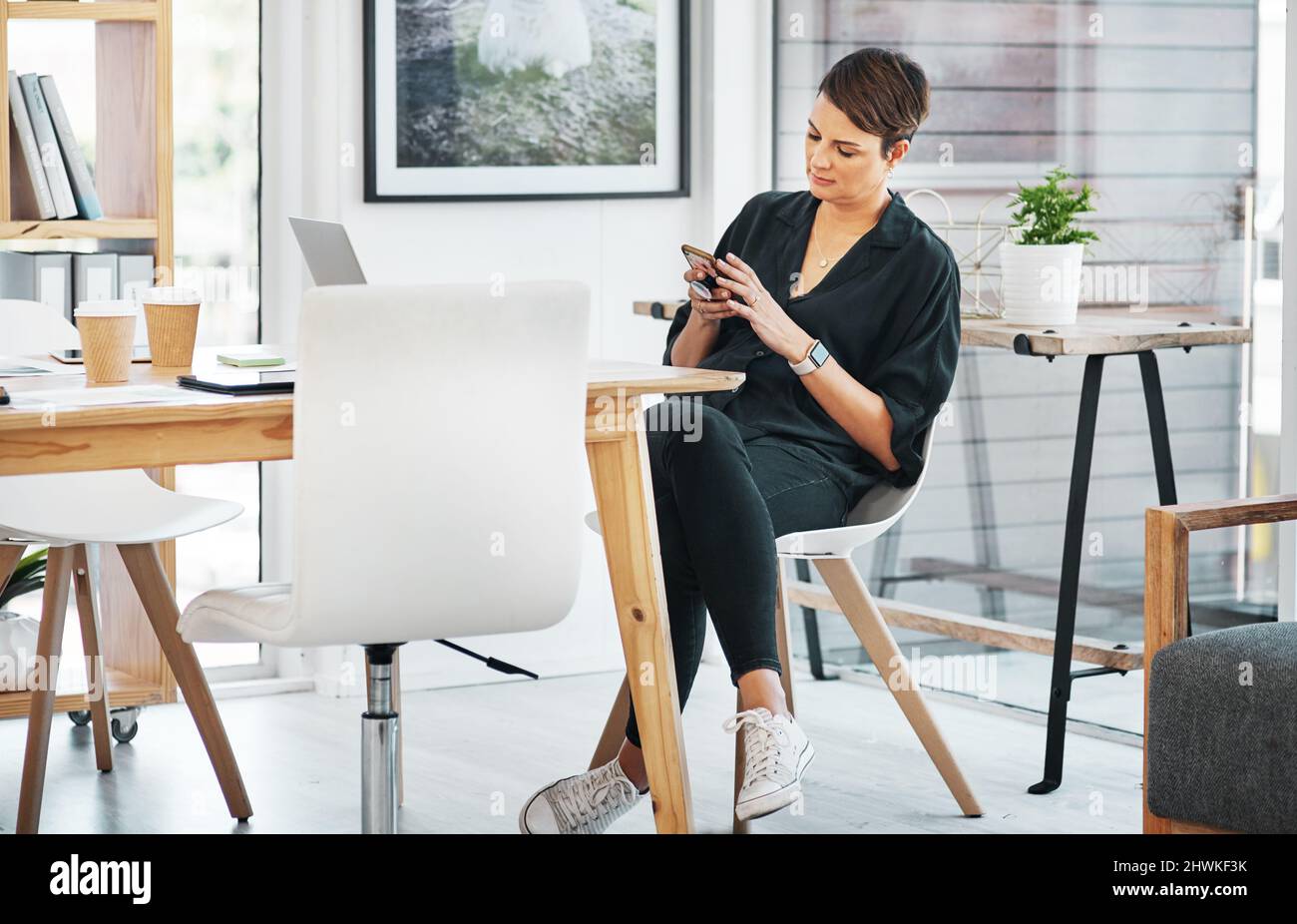 Technology allows me to work from any device. Full length shot of an attractive young businesswoman sitting alone and texting on her cellphone in the Stock Photo