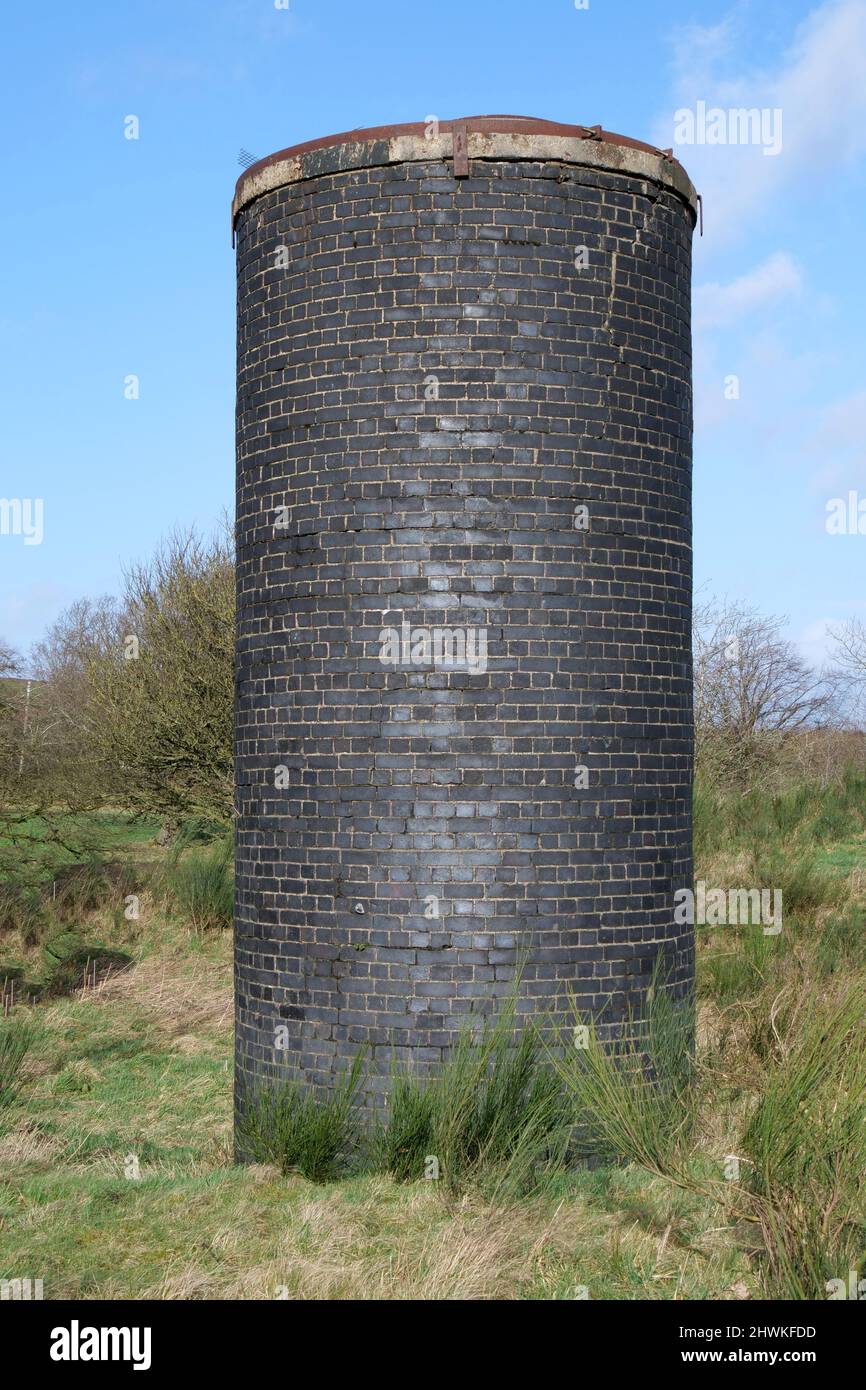 Tall round dark brick built structure among rough overgrown grass Stock Photo