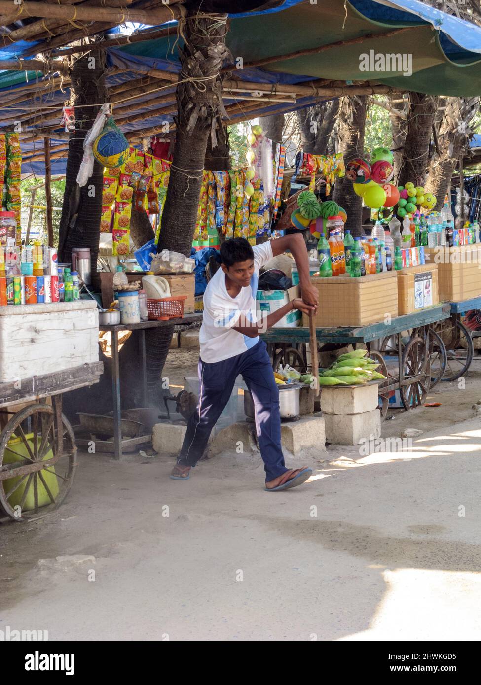India, Gujarat, Island of Diu. A boy playing cricket with a stick in front of his market stall. Stock Photo