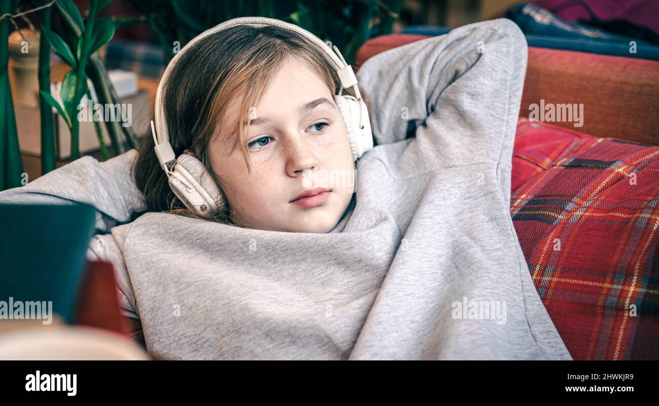 A cute little girl is lying on the couch wearing headphones Stock Photo ...