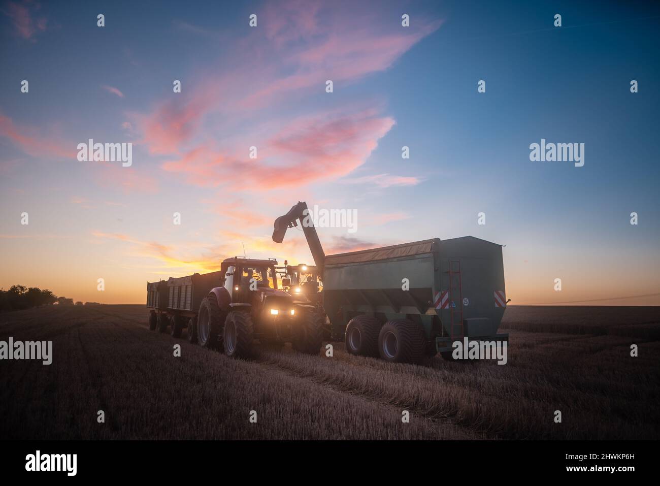 End of a harvest day on a grain field in summer with tractor Stock Photo