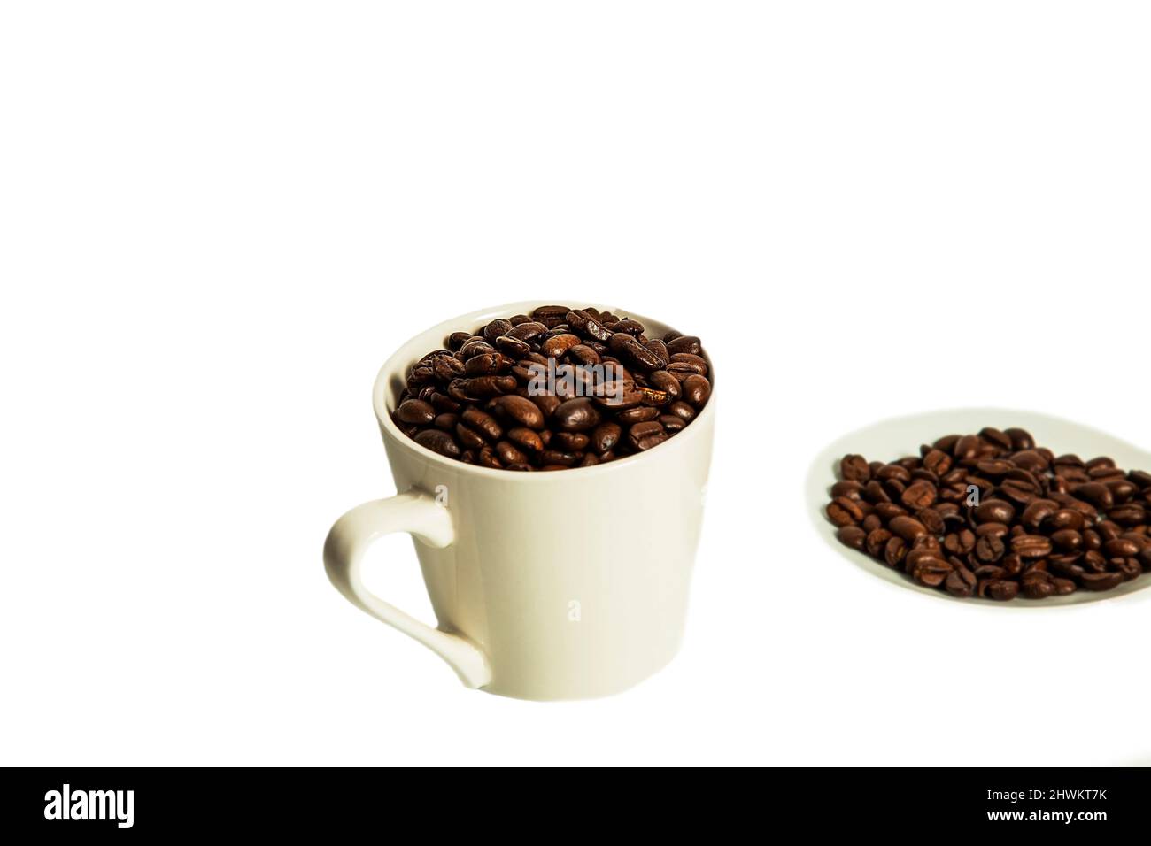 Coffee beans lie in a white mug and saucer on a white background. Isolate. Roasted coffee. Stock Photo