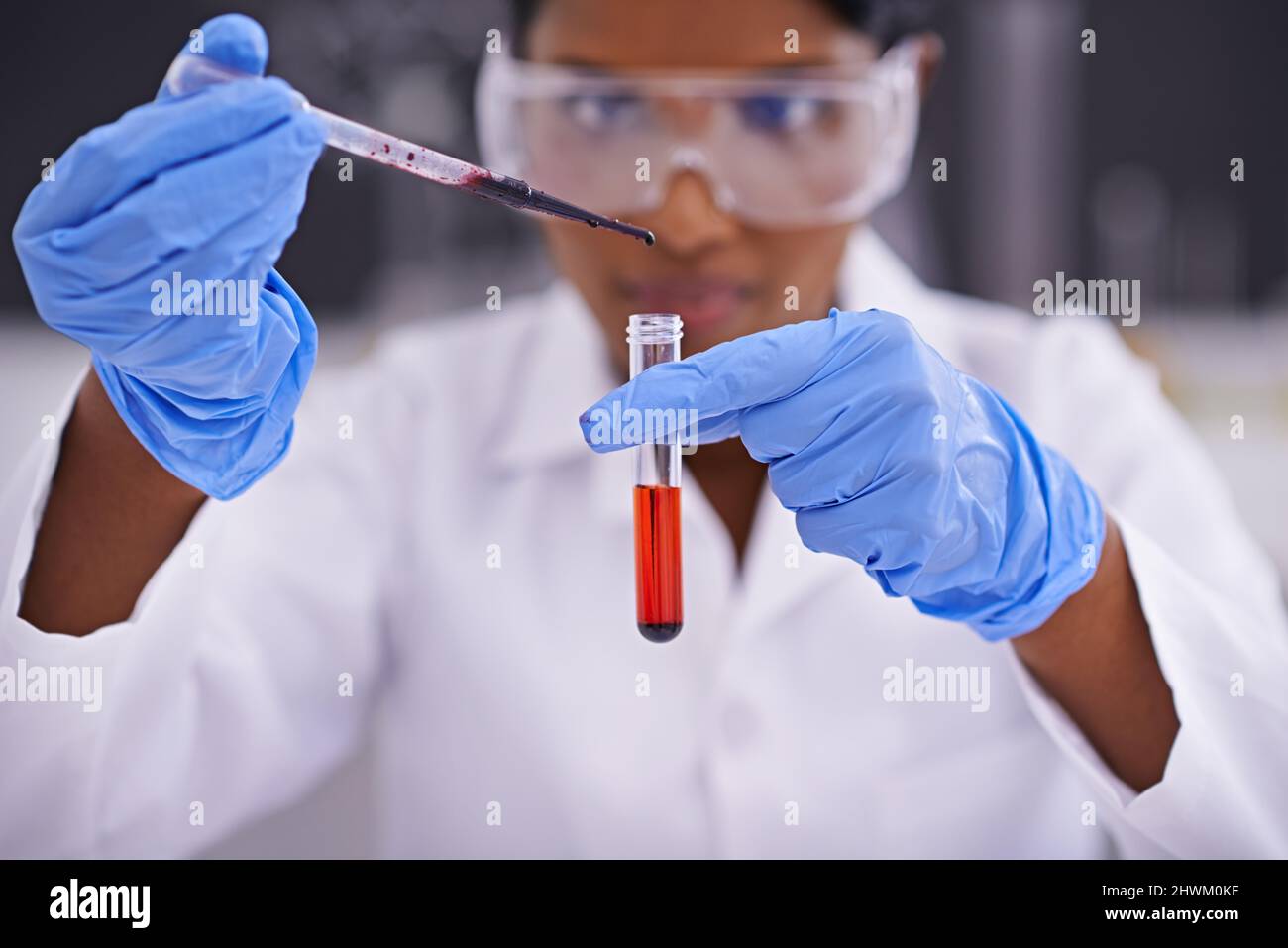 Testing blood samples. A front view of a young scientist dropping a substance into a test tube. Stock Photo