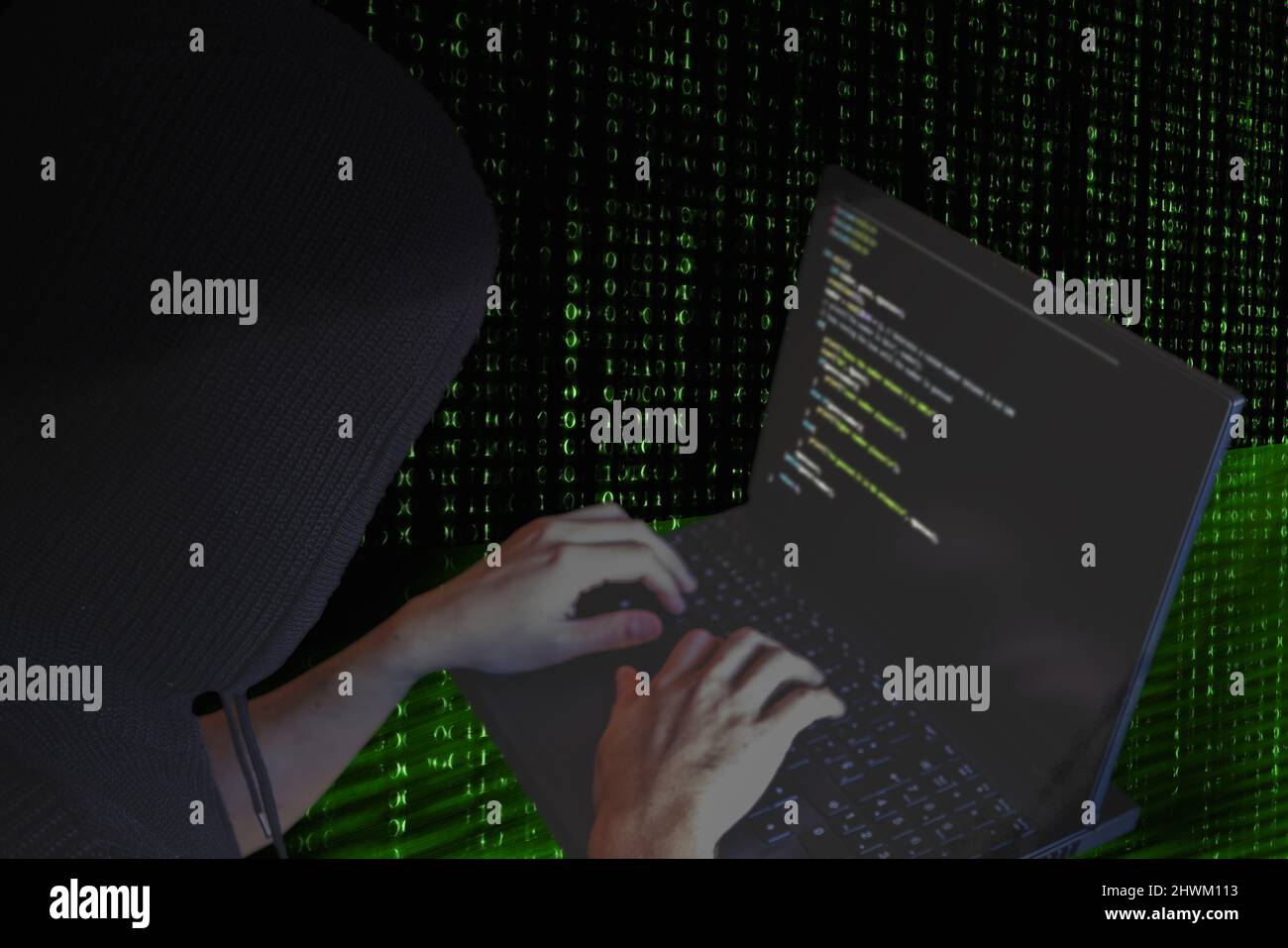 Dark web cyber war concept. Hooded hacker using a laptop for organizing massive data breach attack on government servers Stock Photo