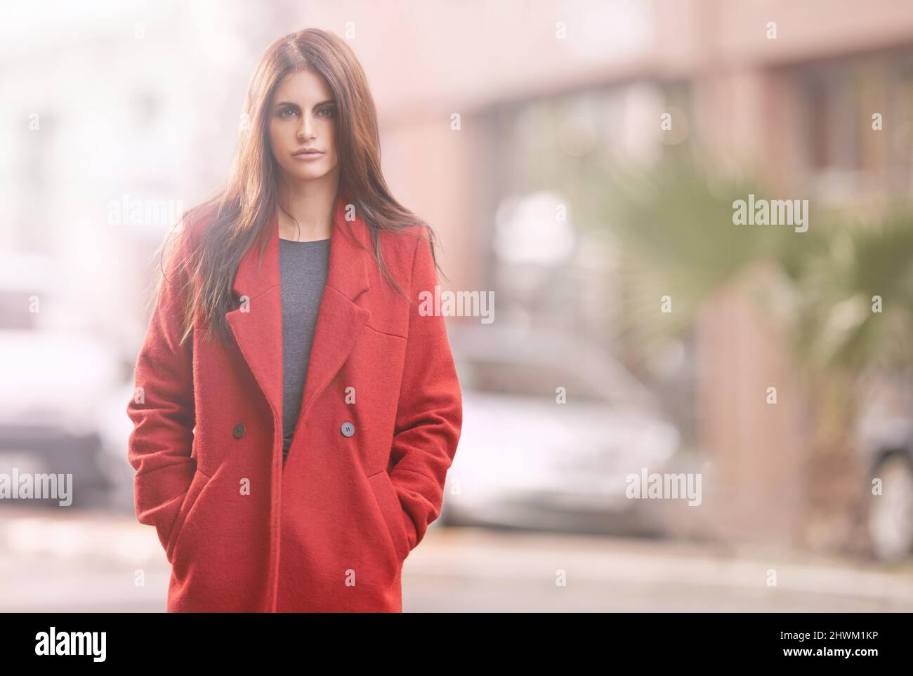 Look fab this fall. Portrait of a gorgeous young woman in a red winter coat standing in an urban setting. Stock Photo