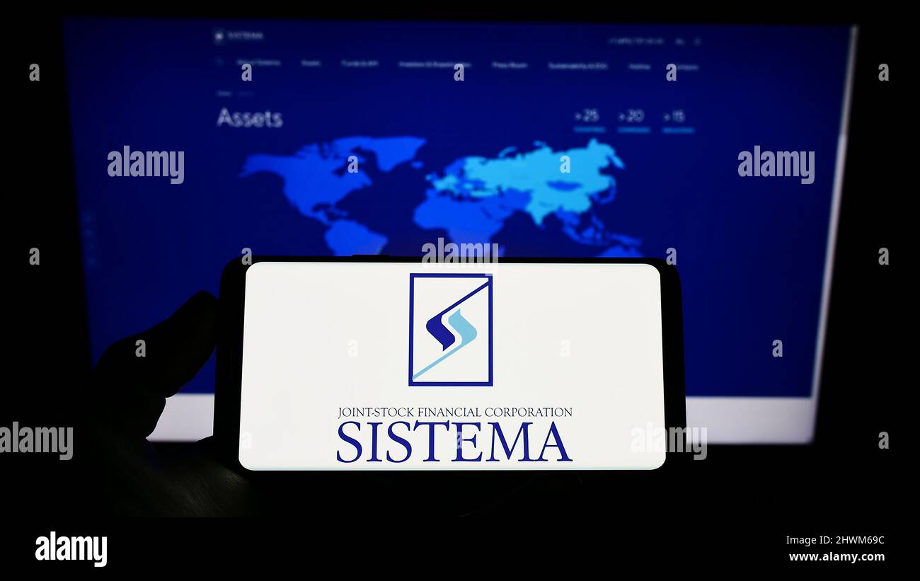 Person holding smartphone with logo of Russian conglomerate AFK Sistema PAO on screen in front of website. Focus on phone display. Stock Photo