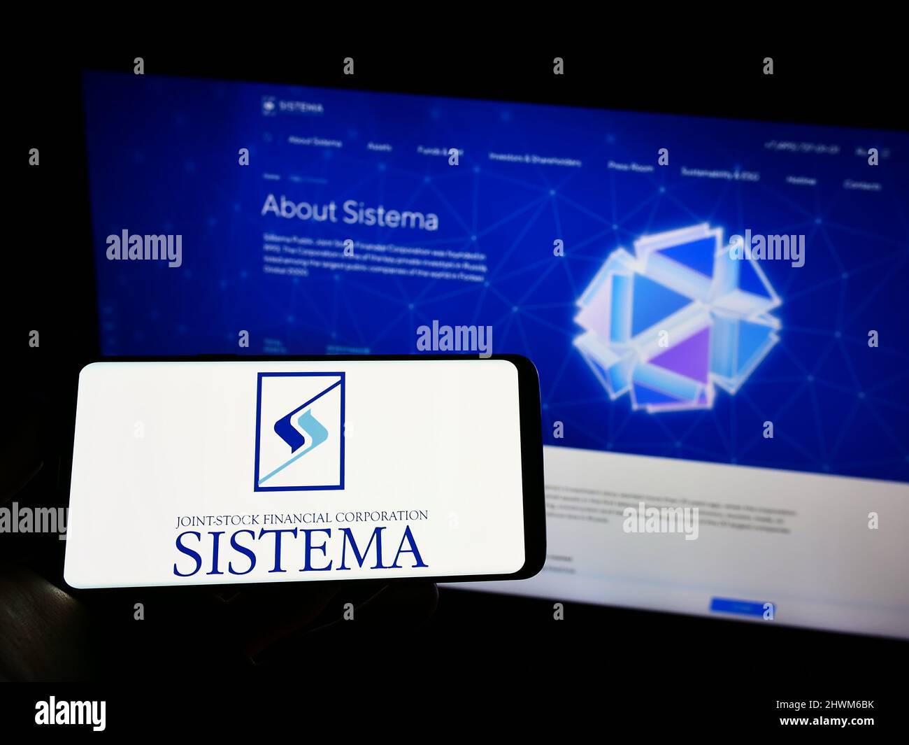 Person holding cellphone with logo of Russian conglomerate AFK Sistema PAO on screen in front of company webpage. Focus on phone display. Stock Photo