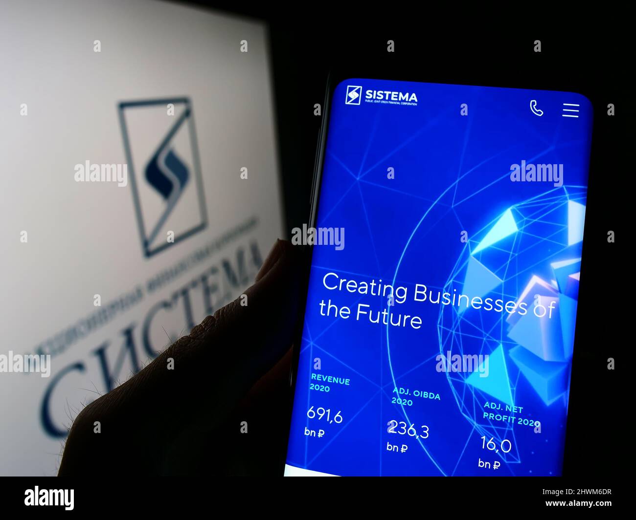 Person holding cellphone with website of Russian conglomerate AFK Sistema PAO on screen in front of logo. Focus on center of phone display. Stock Photo