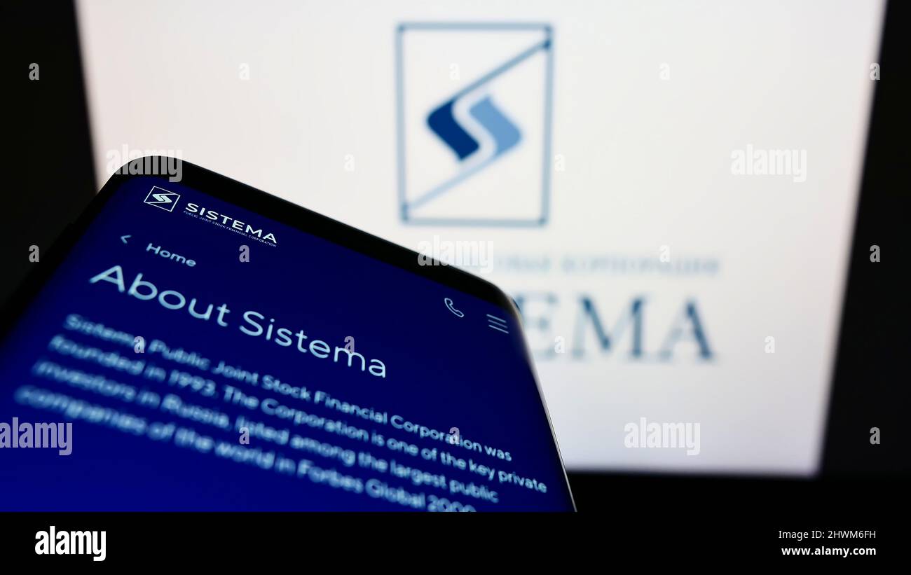 Smartphone with webpage of Russian conglomerate AFK Sistema PAO on screen in front of business logo. Focus on top-left of phone display. Stock Photo