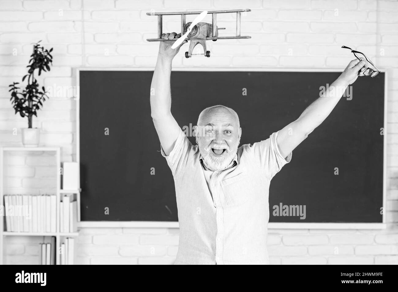 Portrait of excited senior teacher teaching line of high school students with computer laptop in classroom on blackboard. Amazed aged male retired Stock Photo