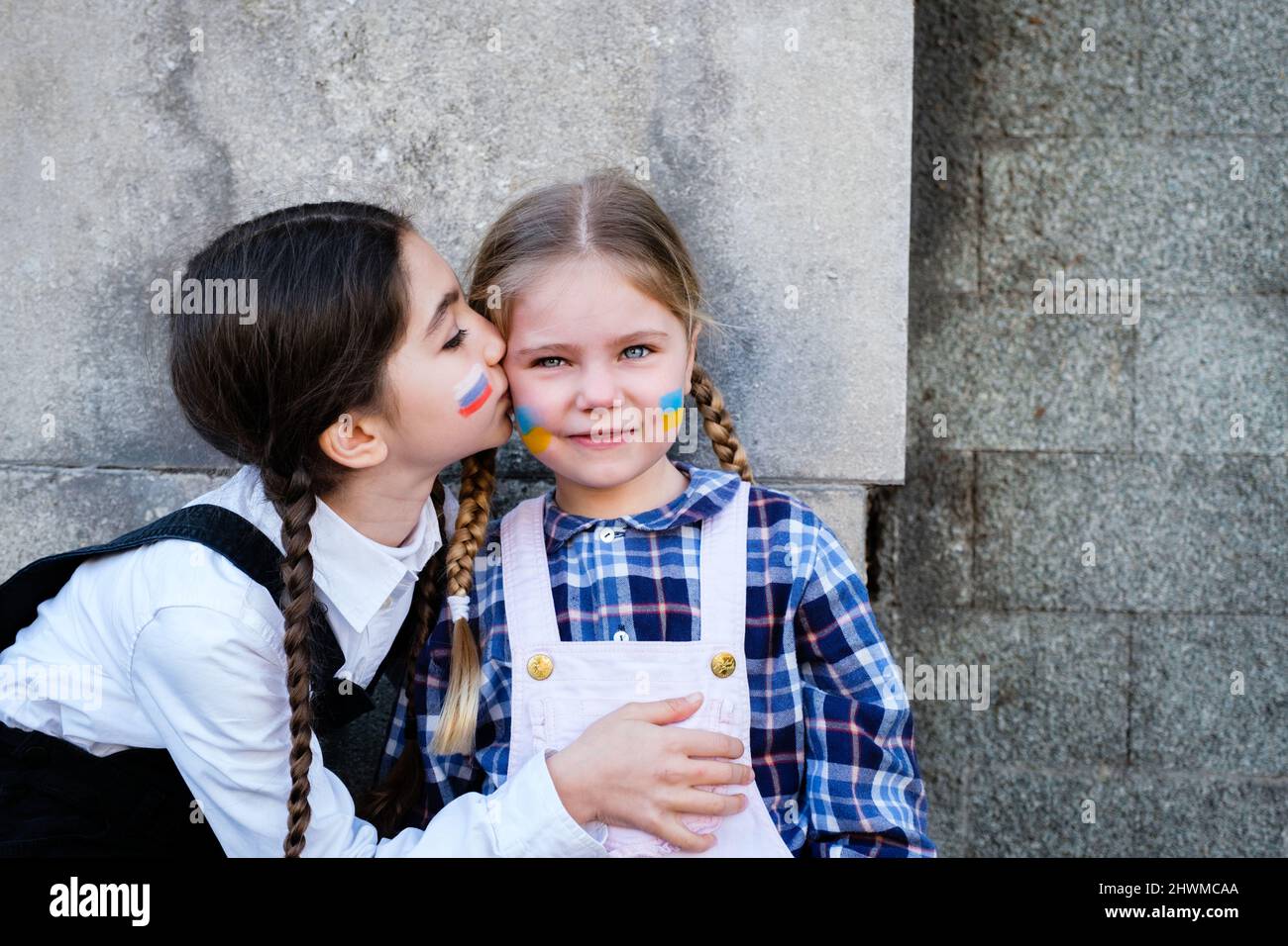 Portrait of two little girls embracing and kissing with Russian and Ukrainian flags on the faces. Concept of peace, stop the war and friendship Stock Photo